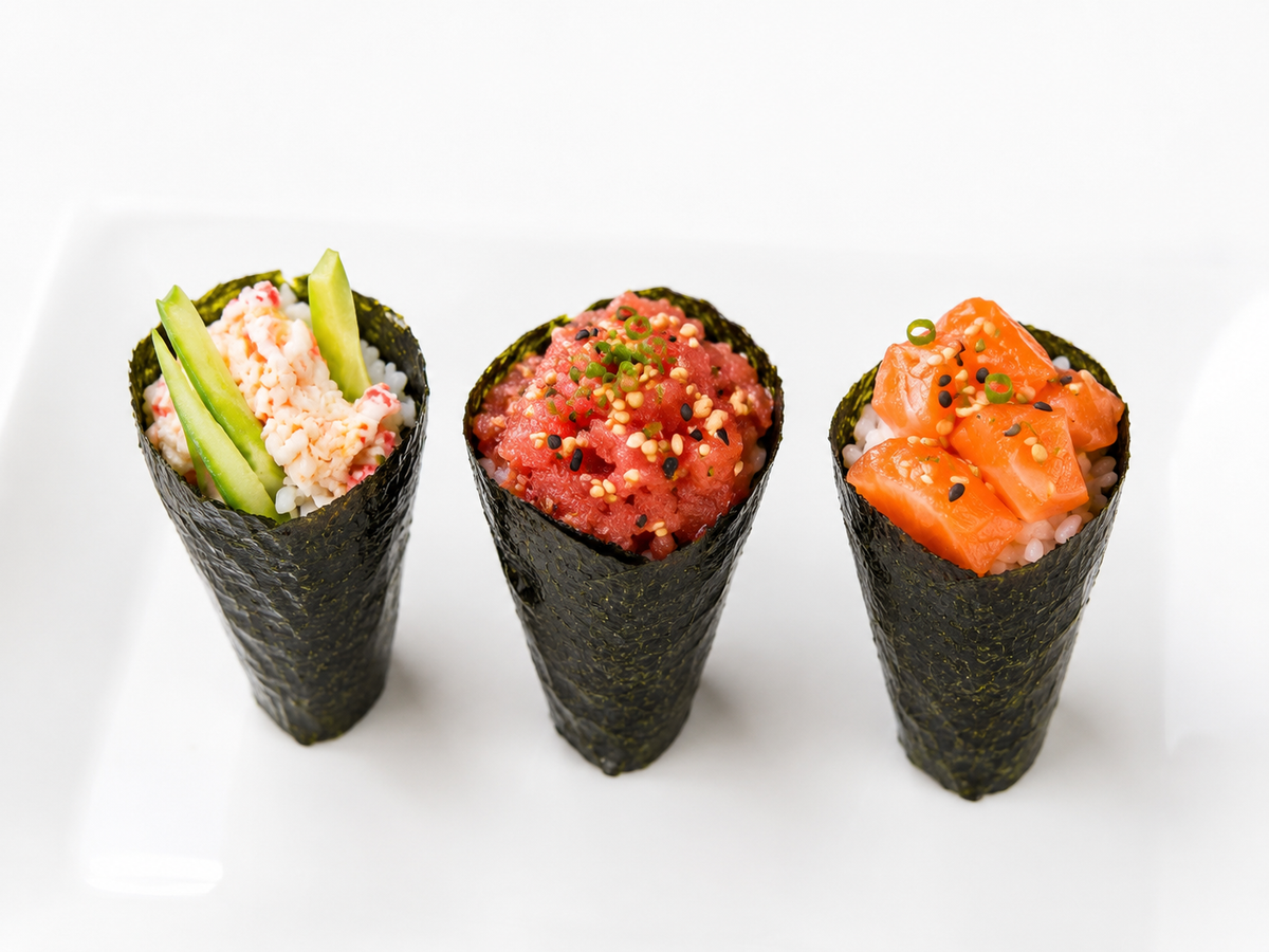 Three types of gourmet sushi cones on a white plate, featuring salmon, tuna, and crab meat with cucumber and sesame seeds.