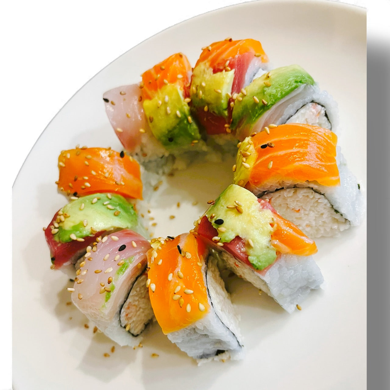 Sushi roll with salmon, avocado, and sesame seeds on a white plate.