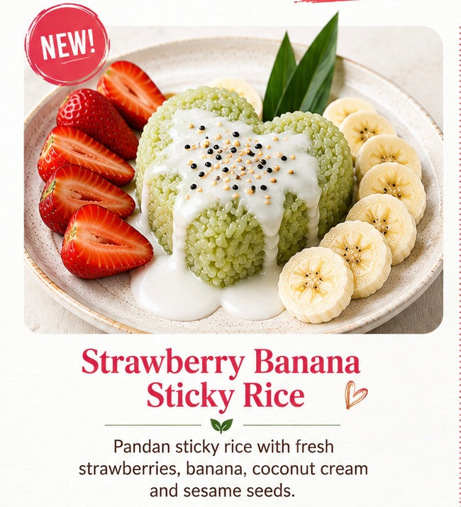 A plated dessert of green sticky rice shaped like a heart, topped with white coconut cream and sprinkled with black and sesame seeds, served with sliced strawberries, banana slices, and a leaf on a light plate. Text below reads 'Strawberry Banana Sticky Rice' with a description of the ingredients.