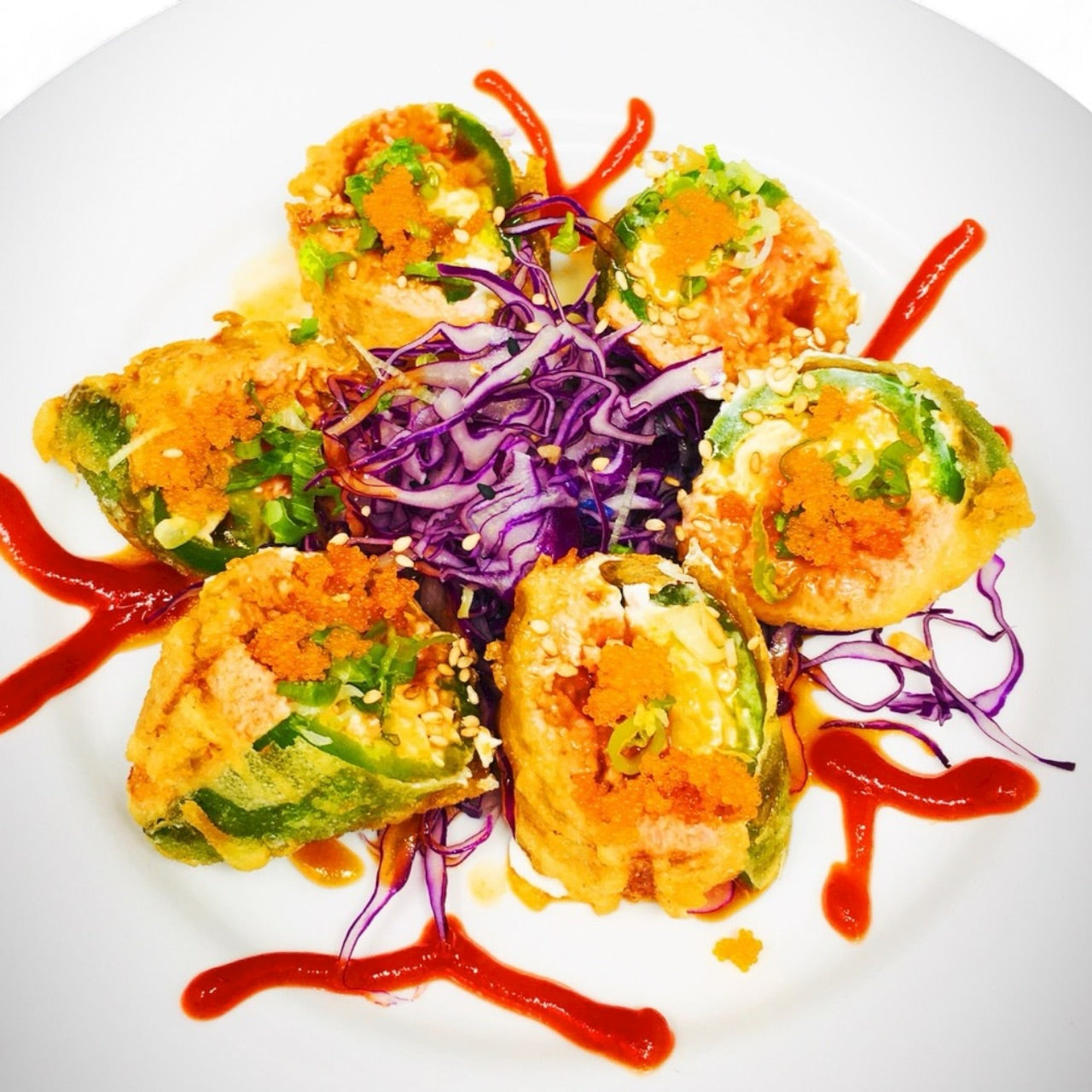 Jalapeno Bomb sushi featuring deep-fried jalapeños stuffed with spicy tuna, masago, and cream sauce, served with shredded purple cabbage and spicy drizzle on a white plate