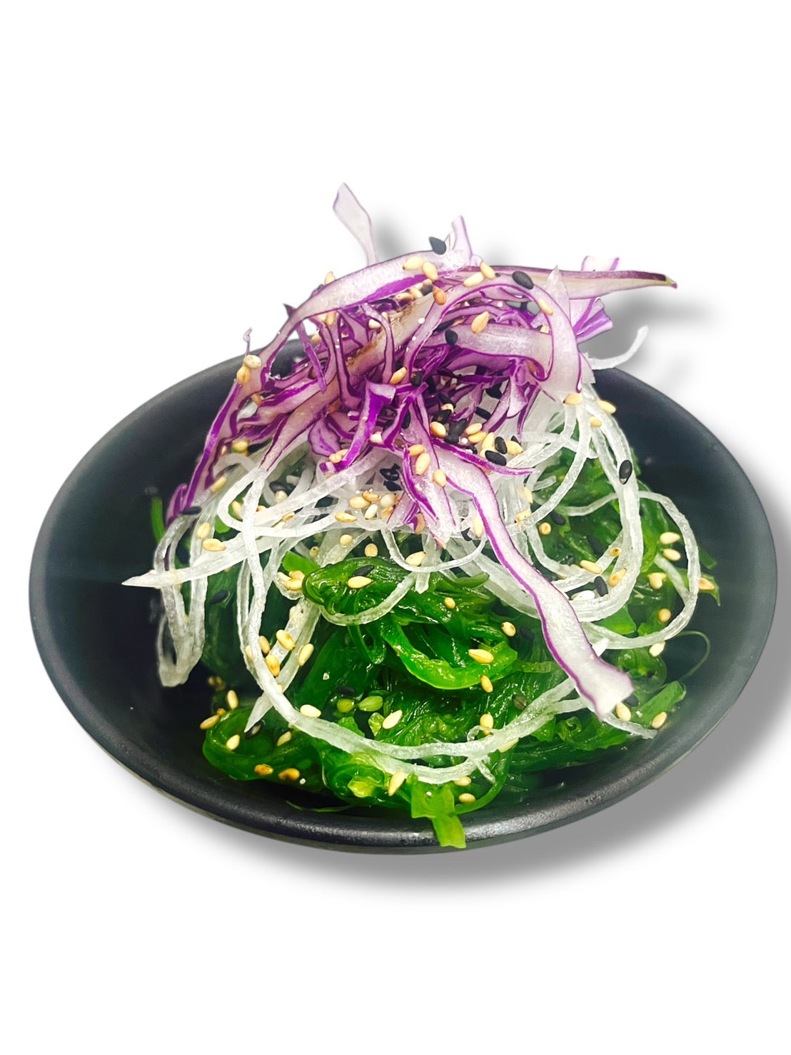 Salad with purple cabbage, green leaves, and sesame seeds on a black plate.
